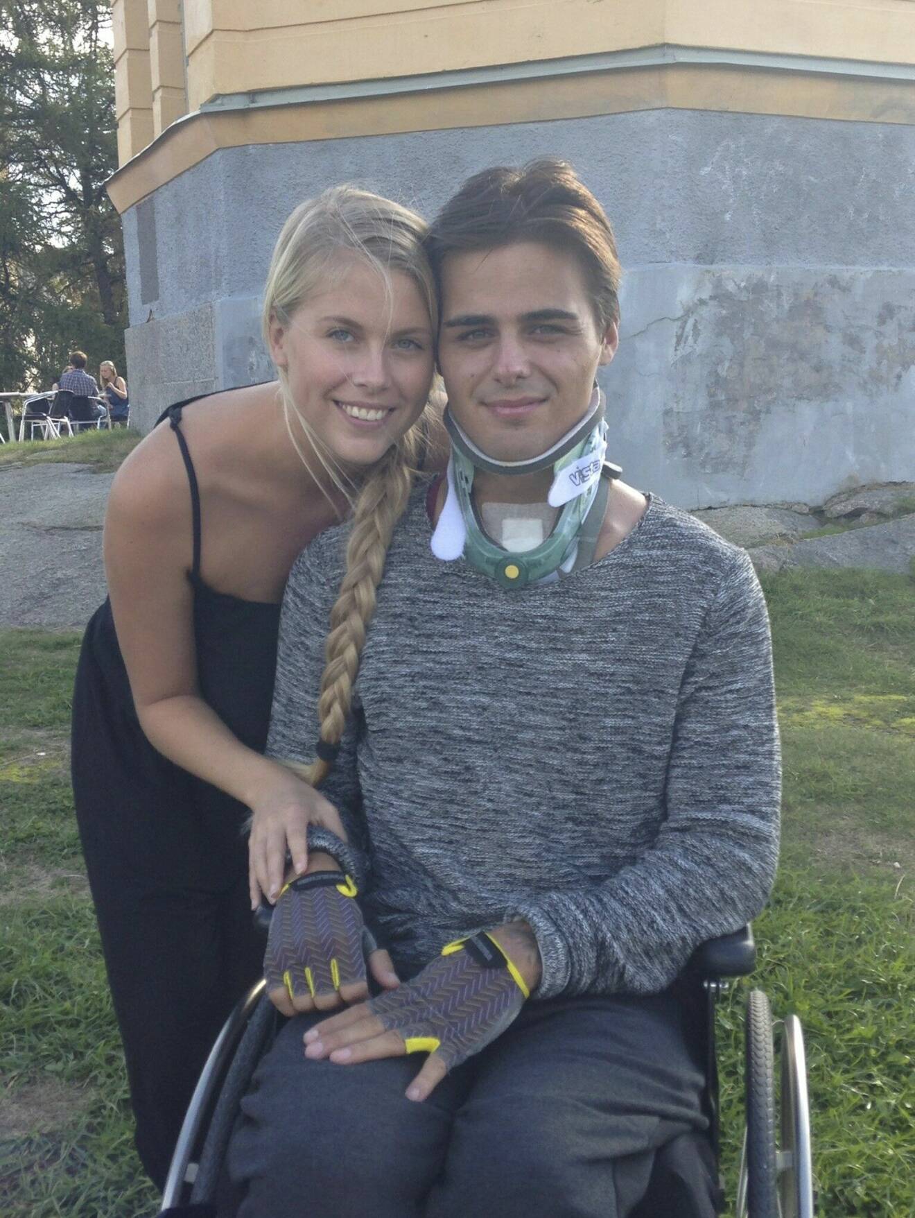 Jonathan Goding Schill en tid efter olyckan, i rullstol, och fortfarande med nackkrage. Josefine Schill finns vid hans sida.