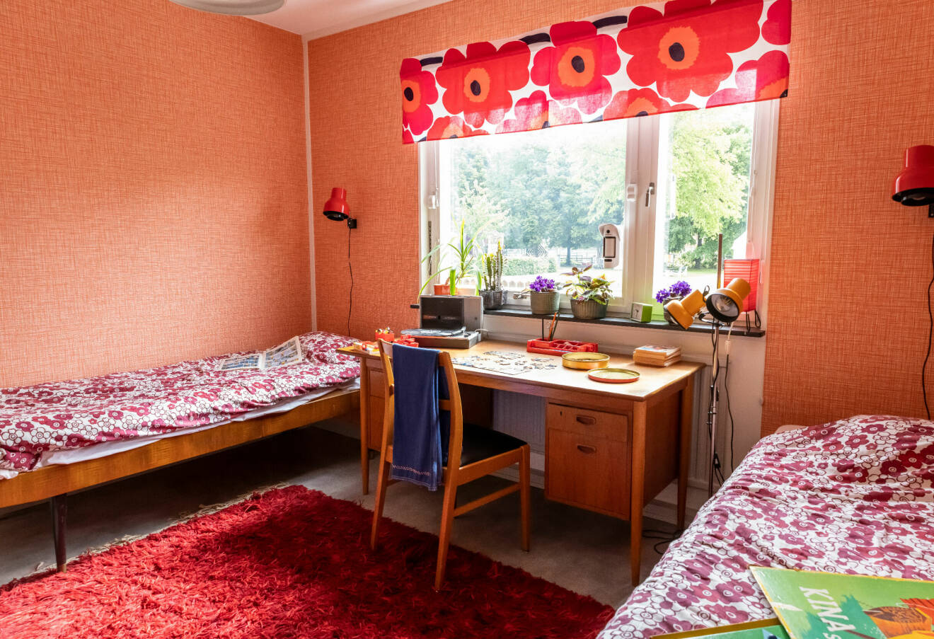 Sovrum i en lägenhet inredd med 70-talsdetaljer. Två sängar står mellan ett skrivbord. I fönstret hängen en gardin sydd i Marimekkotyget Unikko och på golvet en röd ryamatta.