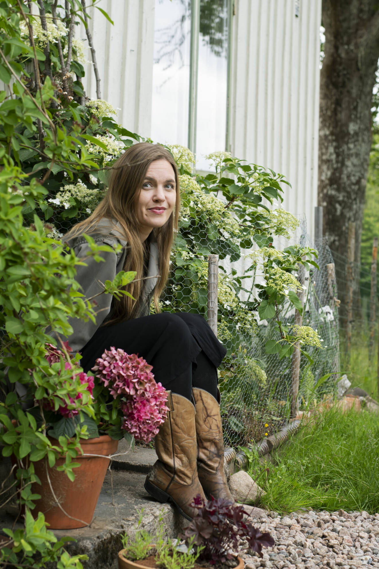 Musikern Ann-Sofie Hoyles sitter vid sitt hus med blommor runt sig.