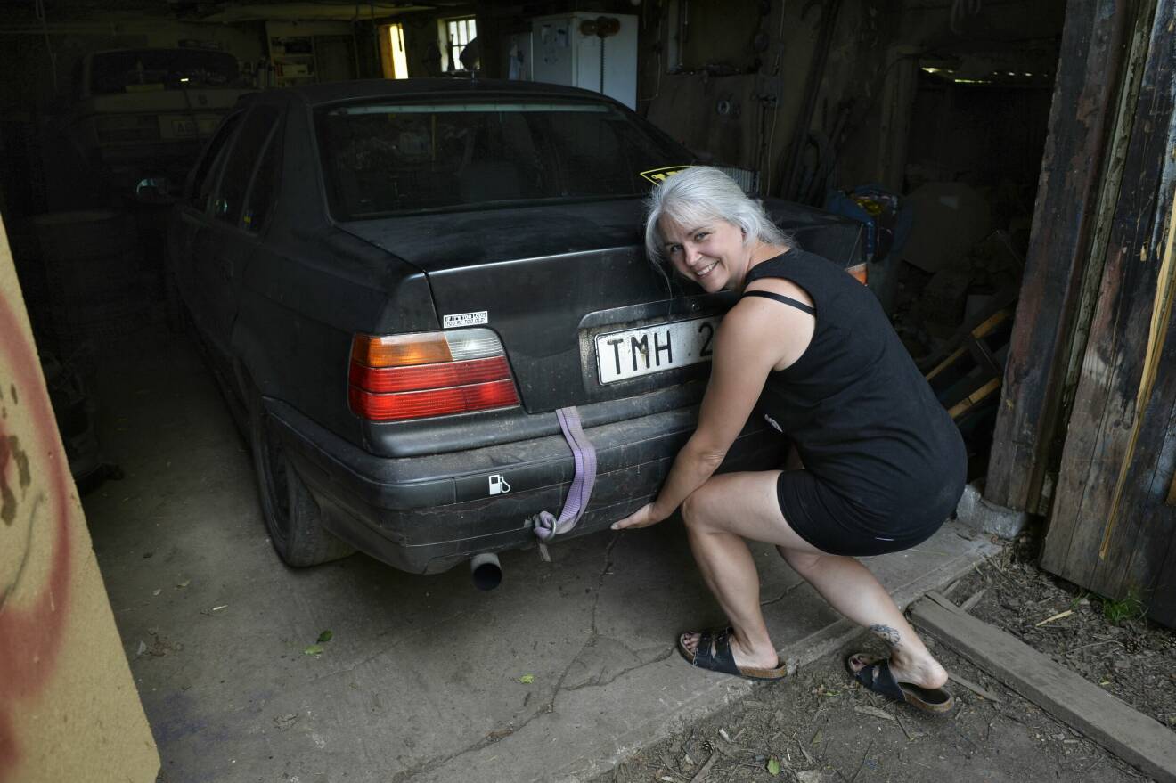 En medelålders kvinna med grått hår låtsas lyfta en bil.