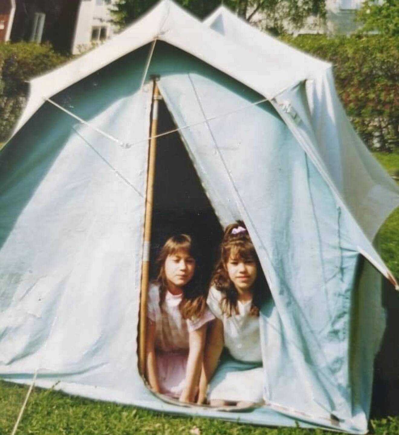 Systrarna Jenny och Johanna sitter på knä i öppningen till ett tält och bilden är tagen när de var barn.