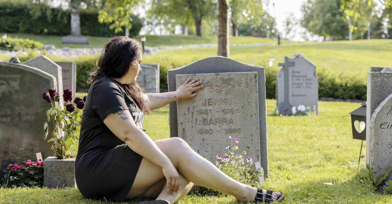 Johanna sitter på gräset framför sina systrar Jenny och Saras grav och håller handen mot gravstenen.