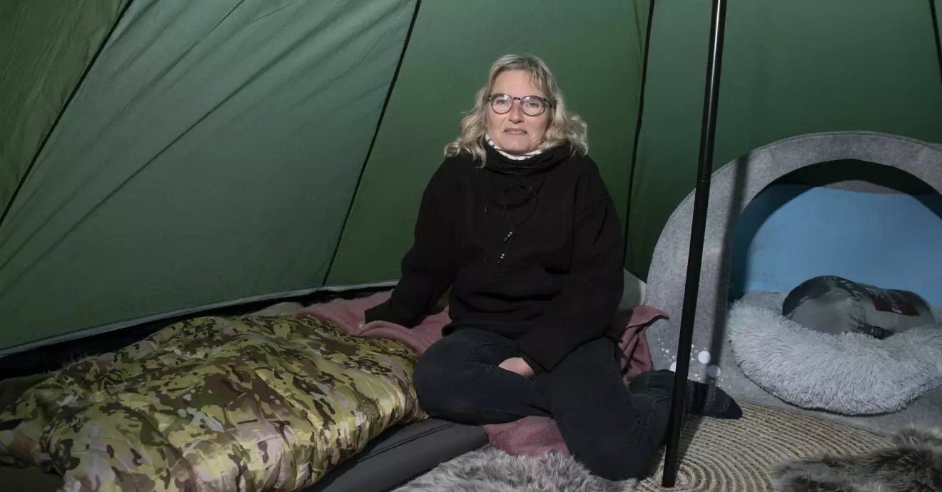 Cana sitter på sin luftmadrass och sovsäck inne i tältet och bredvid henne står en hundkorg.