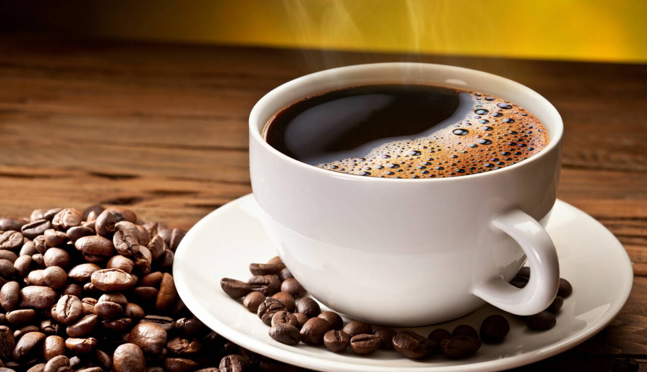 En kopp kaffe som står på ett bord omgiven av kaffebönor.