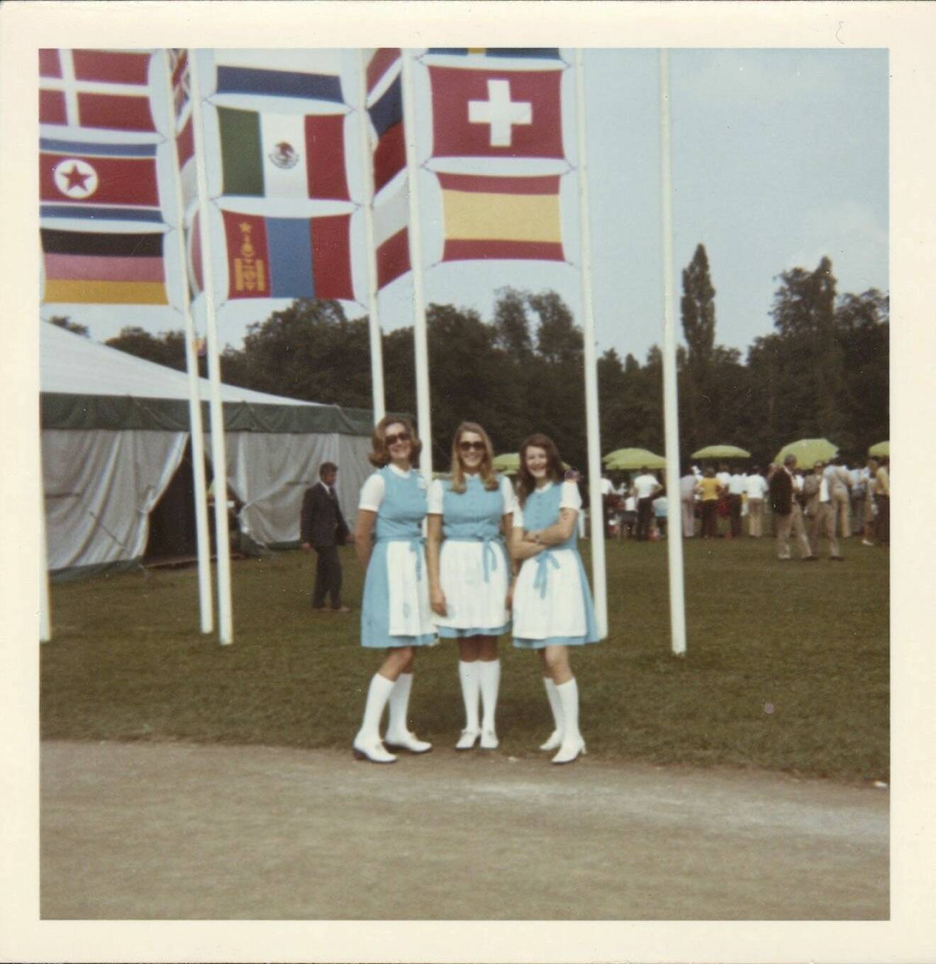 Anna-Sophia von Celsing i sällskap med två andra OS-värdinnor framför en mängd nationsflaggor.