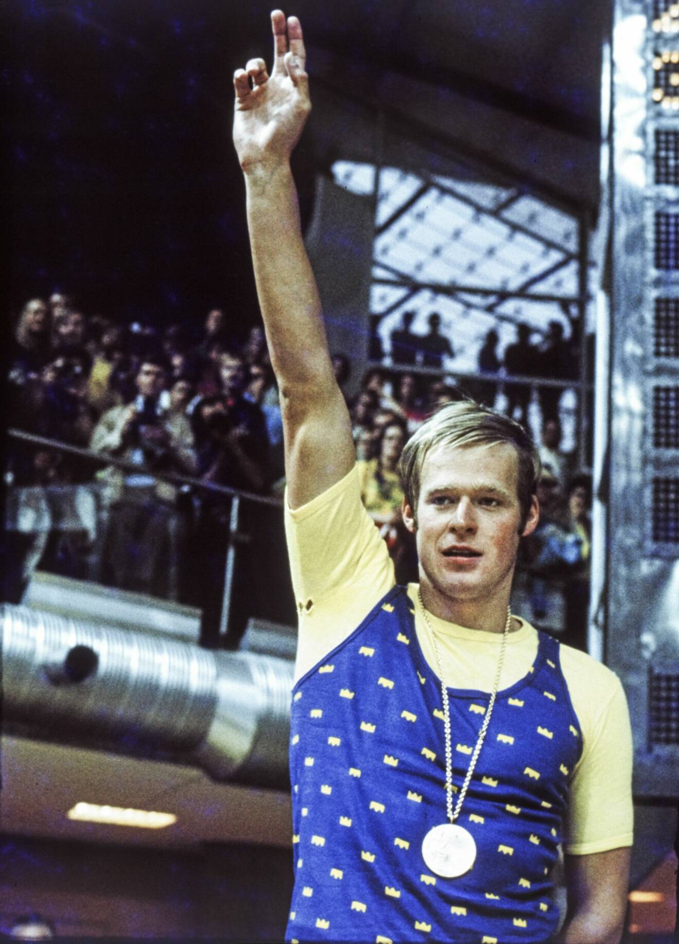 Gunnar Larsson med guldmedalj om halsen höjer armen i en gest mot publiken.