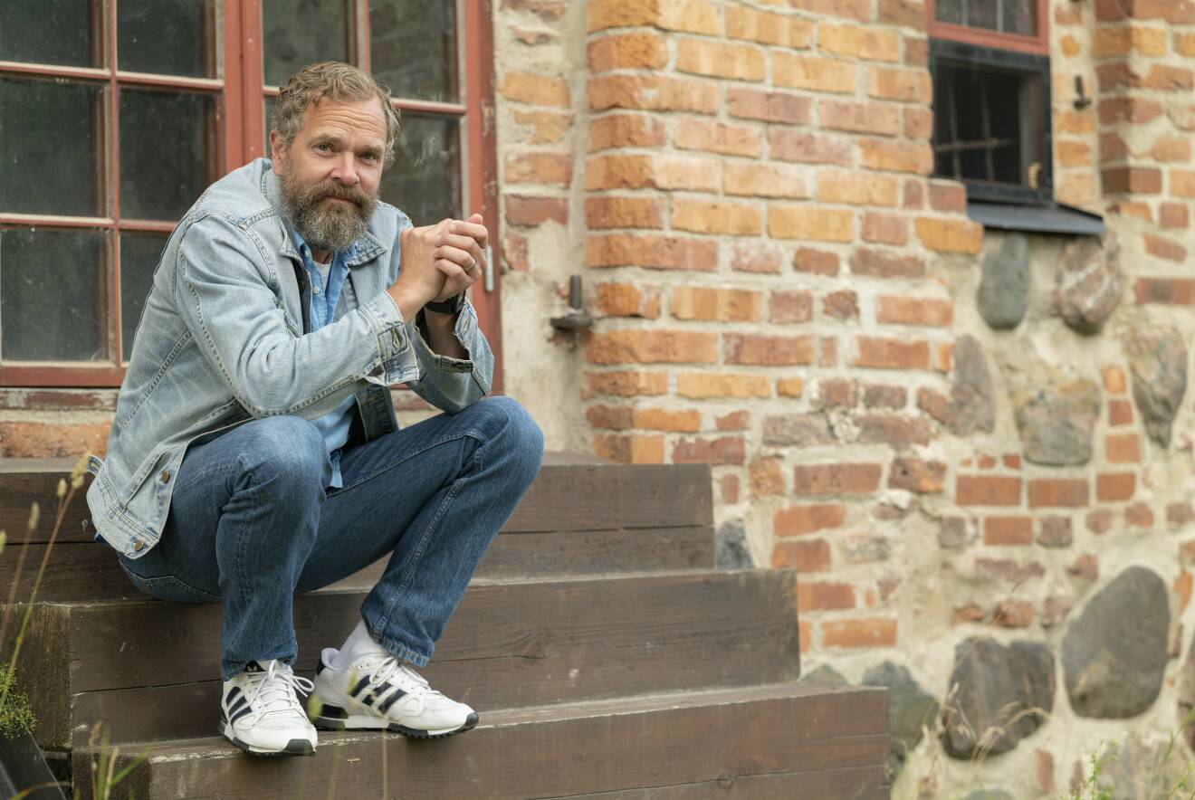 Skådespelaren Per Lasson, som ses i SVT:s dramaserie Tunna blå linjen, sitter på en trappa framför en gammal husvägg i tegel.