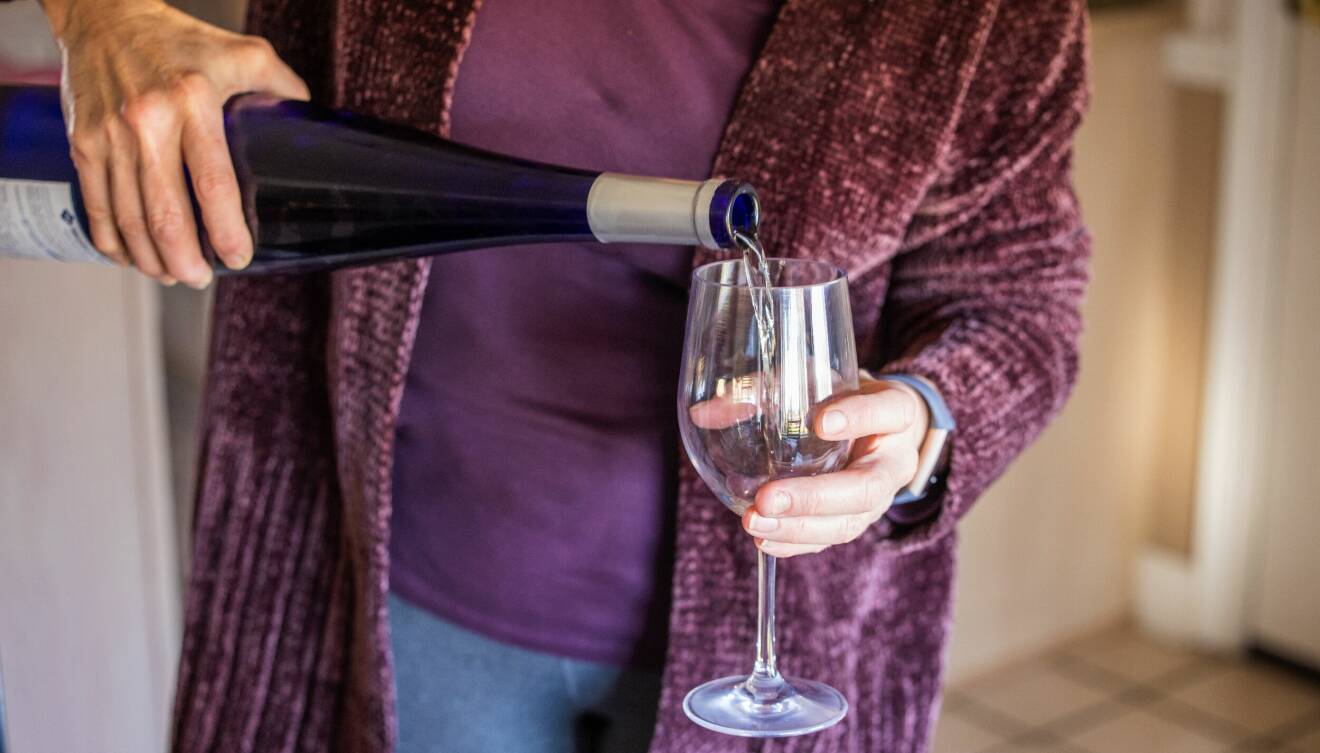 Kvinna håller i vinglas och häller upp vin från flaska som hon håller i andra handen