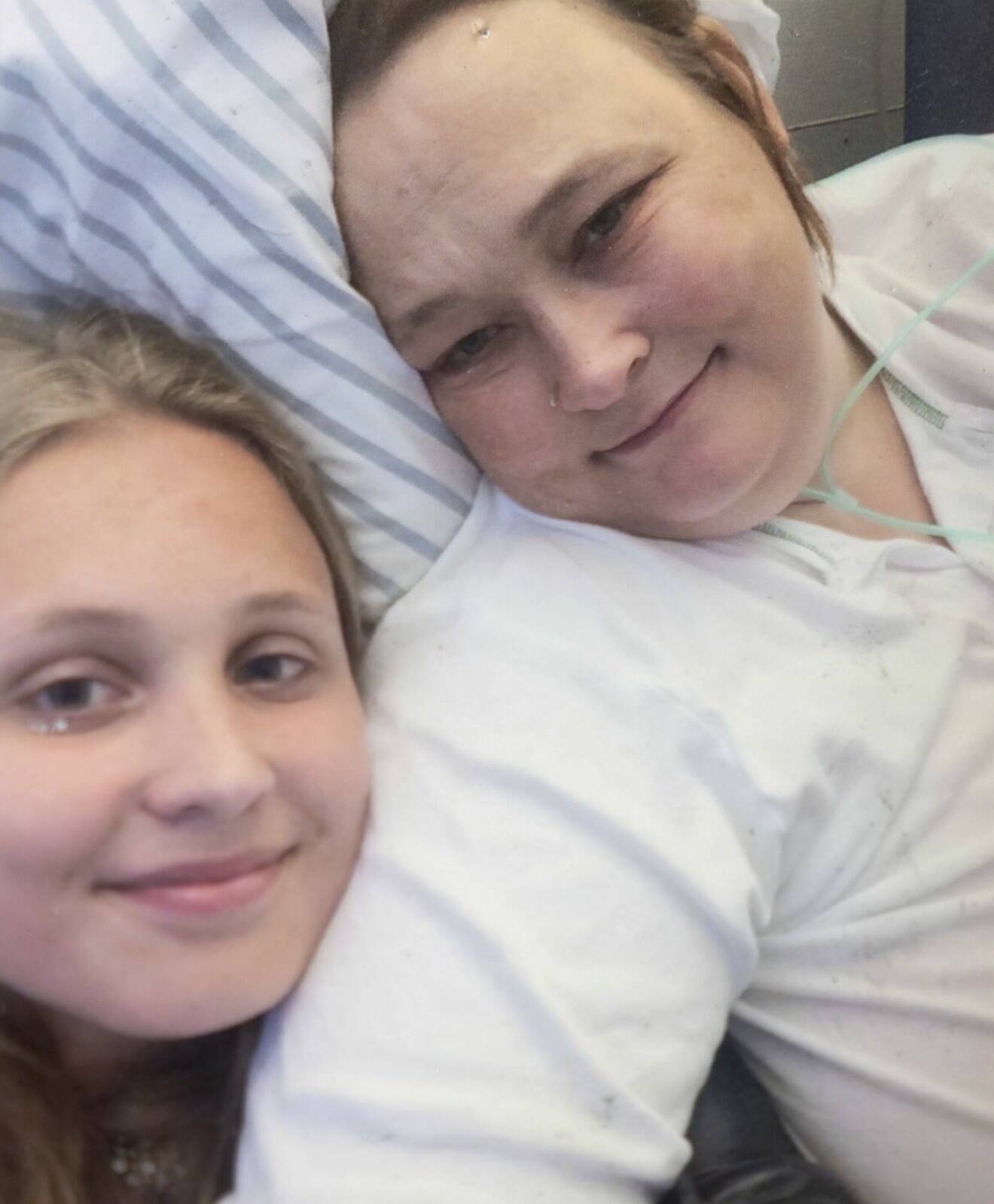 En kvinna i en sjukhussäng med sin tonårsdotter vid sin sida.