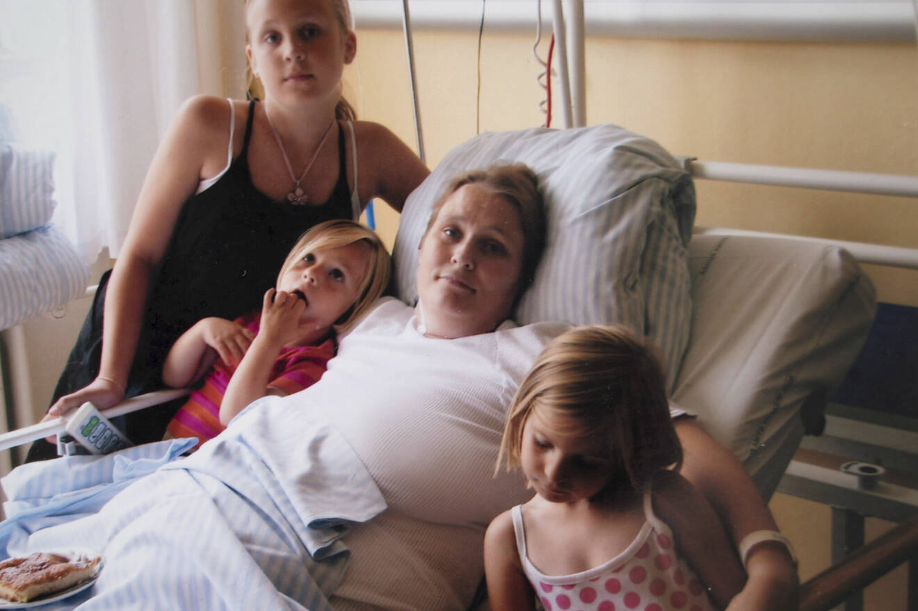 En mamma i en sjukhussäng, omgiven av sina tre små döttrar.