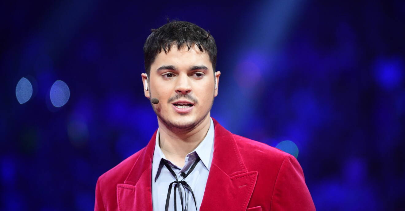 Oscar Zia, iklädd skjorta och röd kavaj, programleder Melodifestivalen.