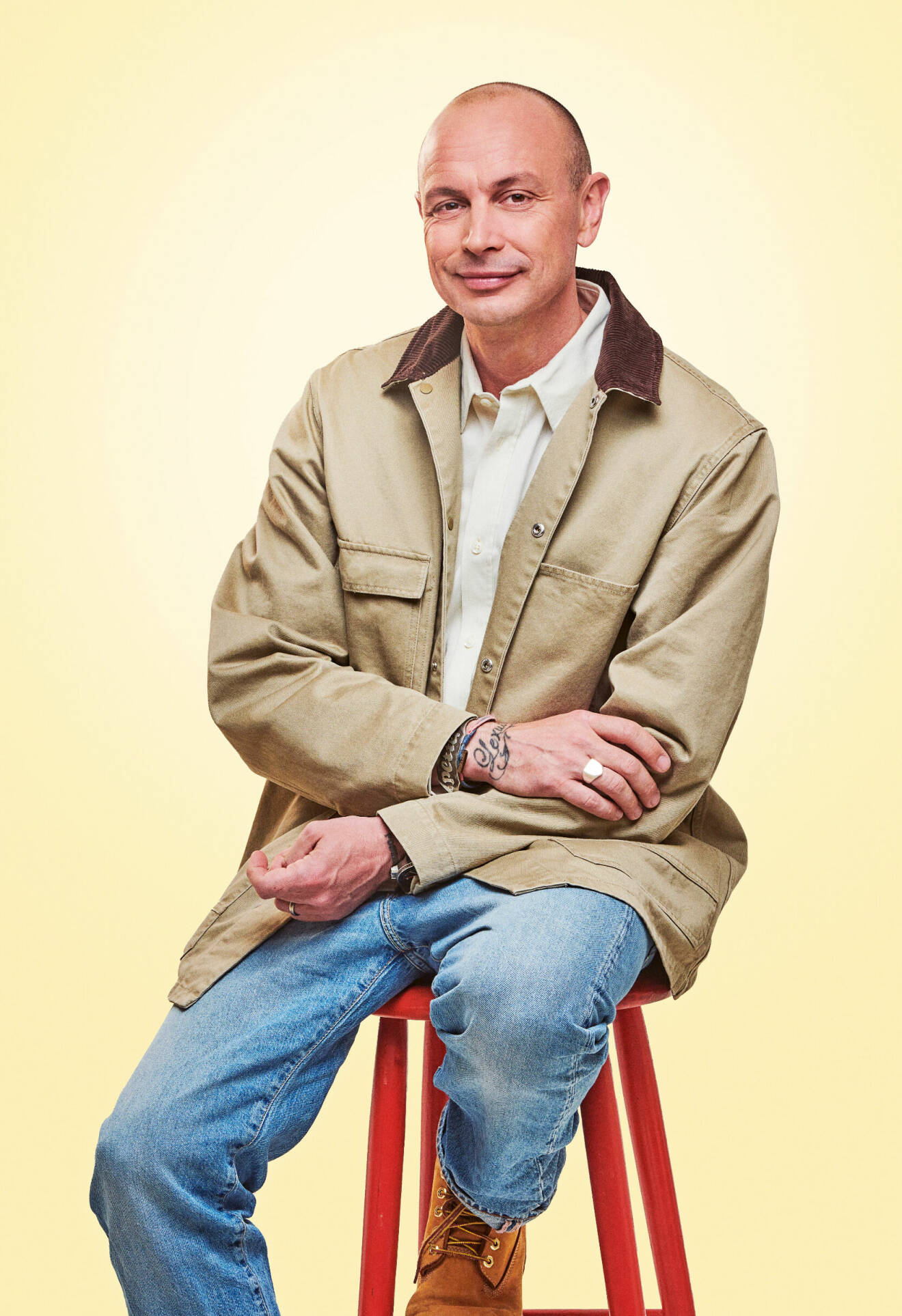 Artisten Petter sitter på en röd pall. Han är klädd i beige jacka, ljus skjorta och jeans.