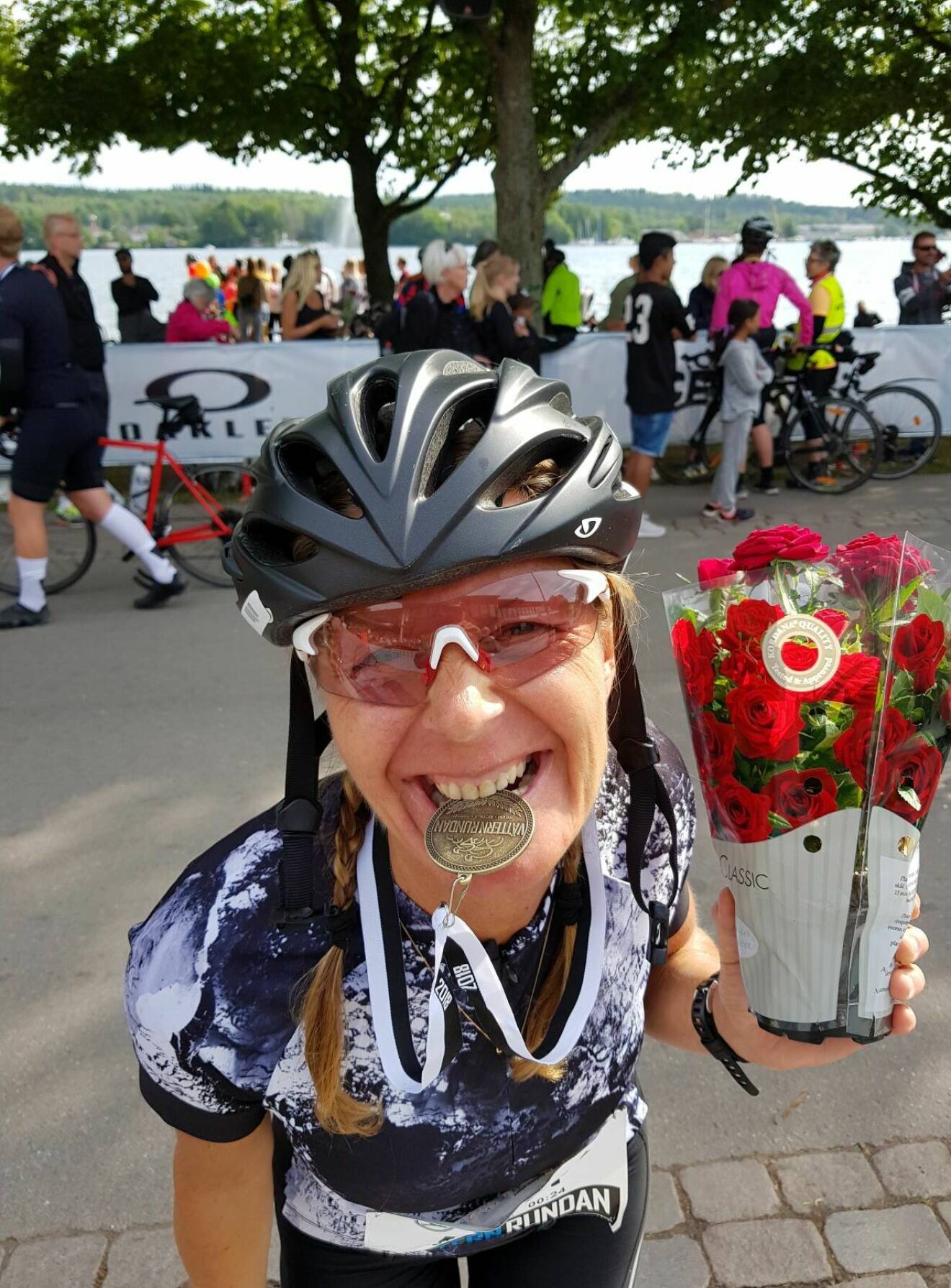Pia Jensen iklädd cykelhjälm och träningskläder, med blomma i ena handen och medalj från Vätternrundan mellan tänderna.