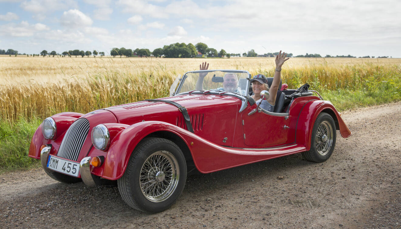 Ett äldre par sitter i en röd, brittisk sportbil av äldre modell.