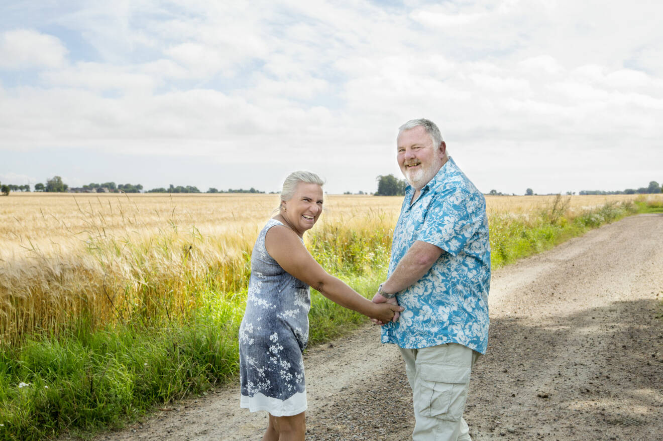Ett äldre par håller varandra i handen på en grusväg vid ett skånskt sädesfält.