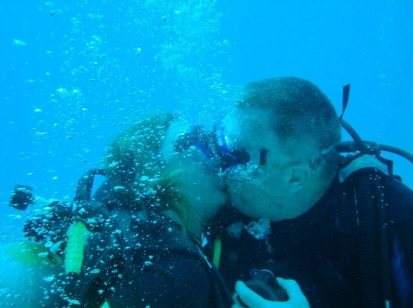 Ett par i dykarutrustning pussar varandra under ytan.