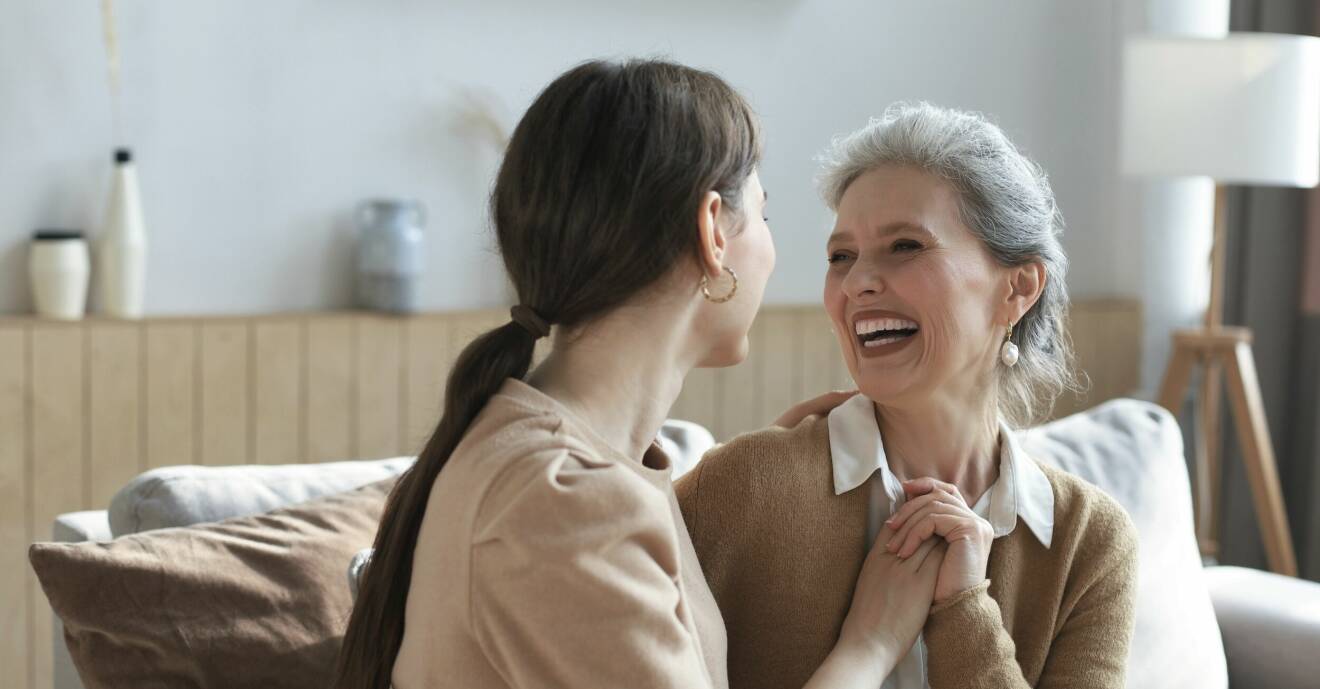 En yngre och en äldre kvinna skrattar tillsammans i en soffa