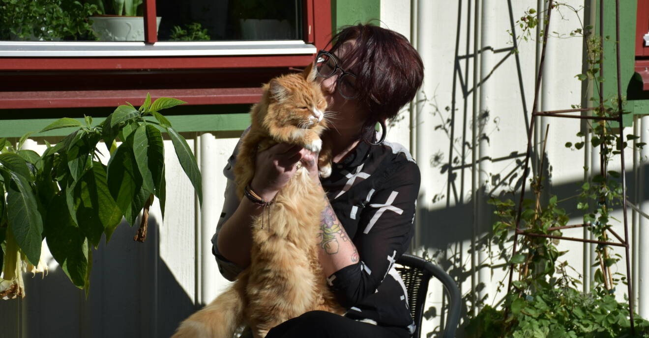Sandra Lundberg sitter utanför ett trähus och håller en katt i famnen.