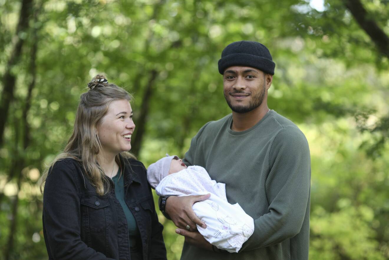 Andréa Sunna tillbaka i Sverige med maken Paluki från Tonga, och dottern Maleah som är född i Sverige. Familjen står utomhus med träd i bakgrunden.