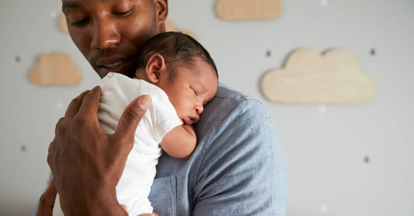 Nybliven pappa håller sin sovande bebis mot bröstet.