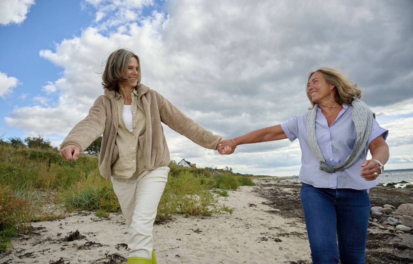 Birgitta Hågemark Olshov och Annika Erlandsson Olshov går hand i hand på stranden i Viken vid Öresund.