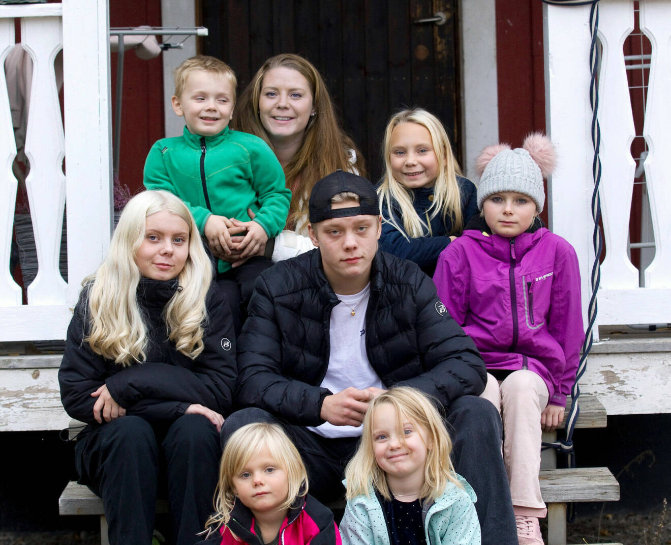 Porträttbild på Emma med sina sex barn, Stina, Sally, Svea, Saga, Silla och Saxon. Samt systerbarnen Ebba och Kevin. De sitter på trappen utanför huset.