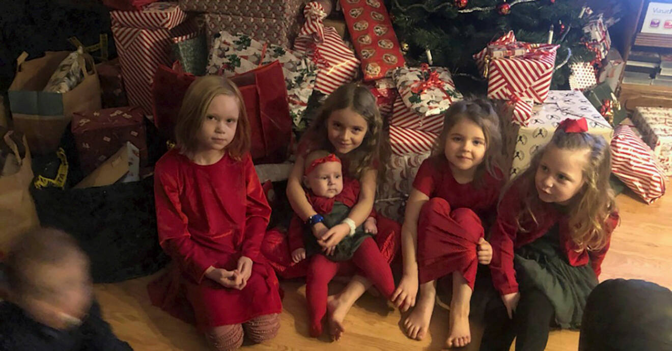 Fem av Irens barnbarn och bonusbarn sitter på golvet framför en stor hög med julklappar som ligger framför en julgran.