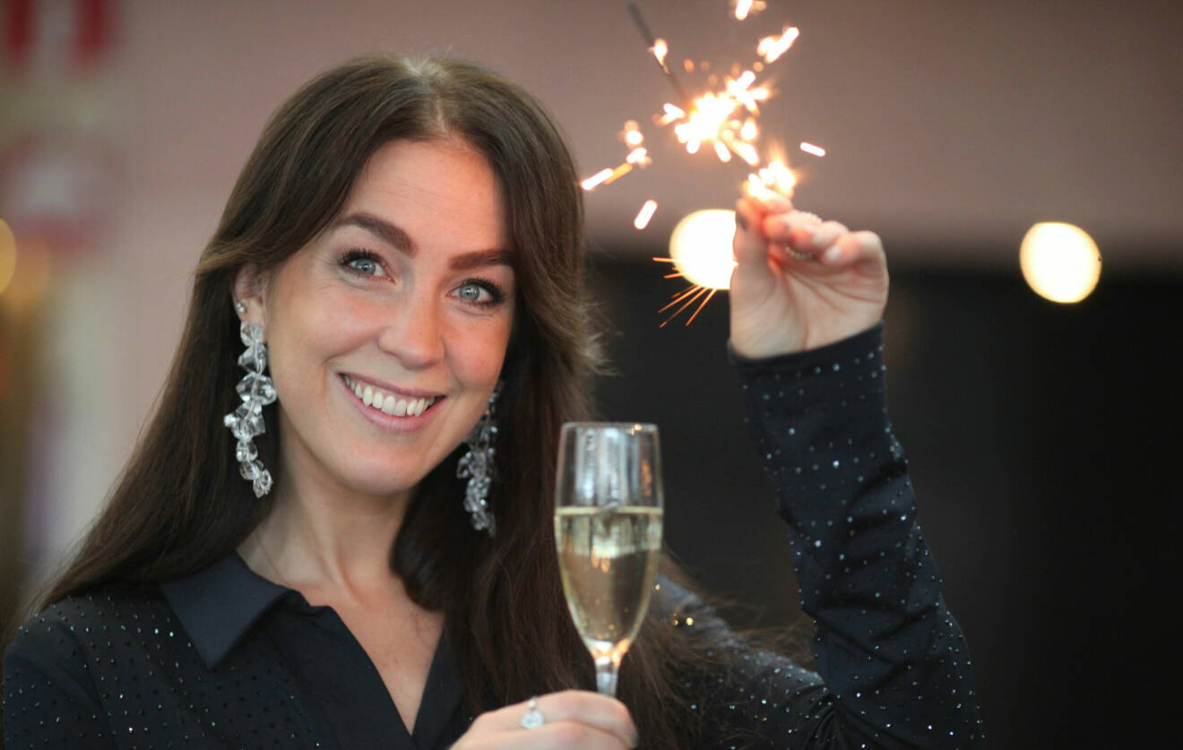Porträttbild på Sofia. Hon har stora silvriga örhängen på sig, håller i ett glas med champagne i ena handen och ett brinnande tomtebloss i den andra.