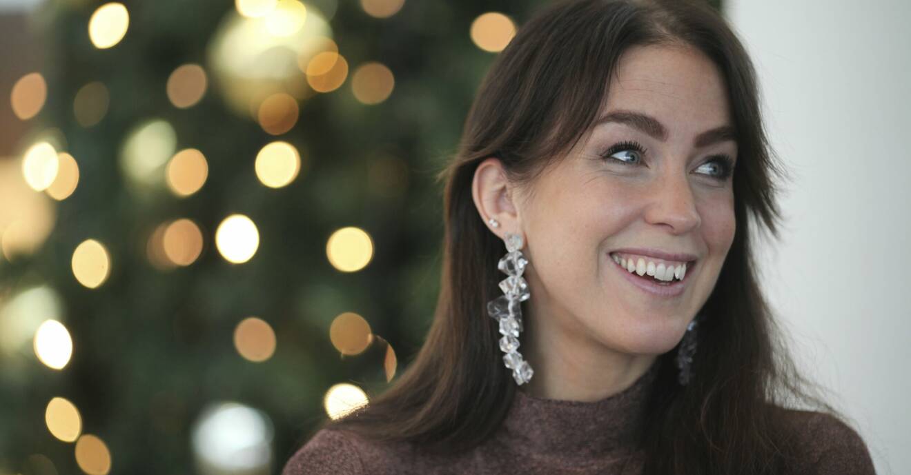 Porträttbild på Sofia. Hon har stora silvriga örhängen på sig och tittar ut ur bilden och ler. I bakgrunden syns en julgran.