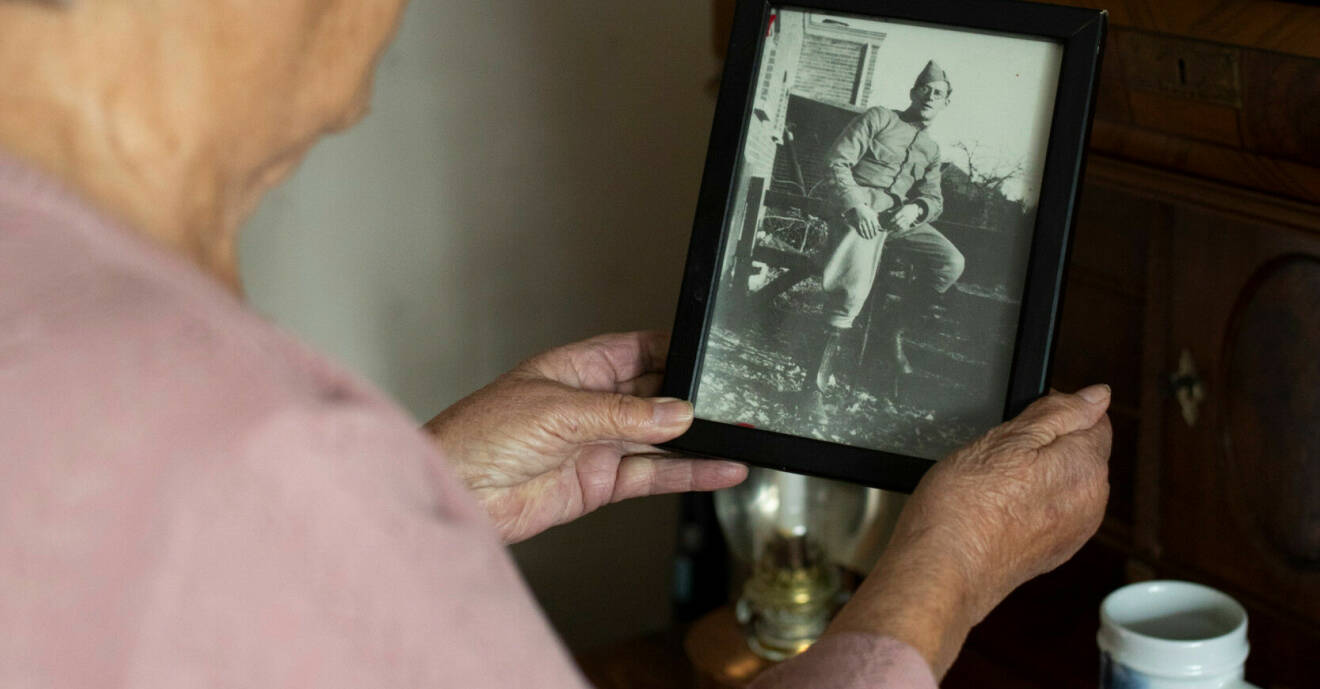 Jopie syns suddigt i förgrunden och håller upp ett gammalt svartvitt fotografi på sin pappa i handen.
