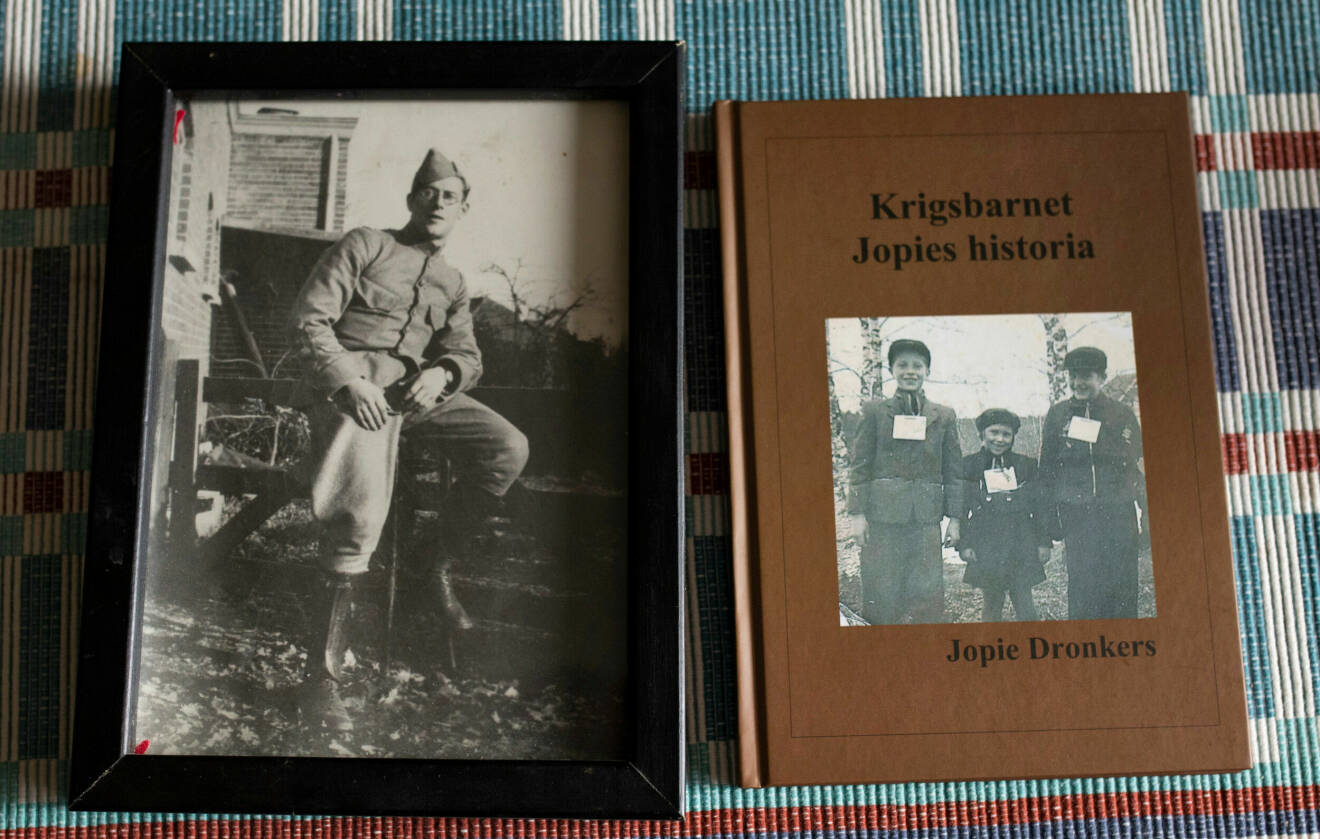Bild på ett gammalt svartvitt fotografi på Jopies pappa och Jopies nya bok "Krigsbarnet Jopies historia". Omslaget på boken är brunt med ett svartvitt fotografi.