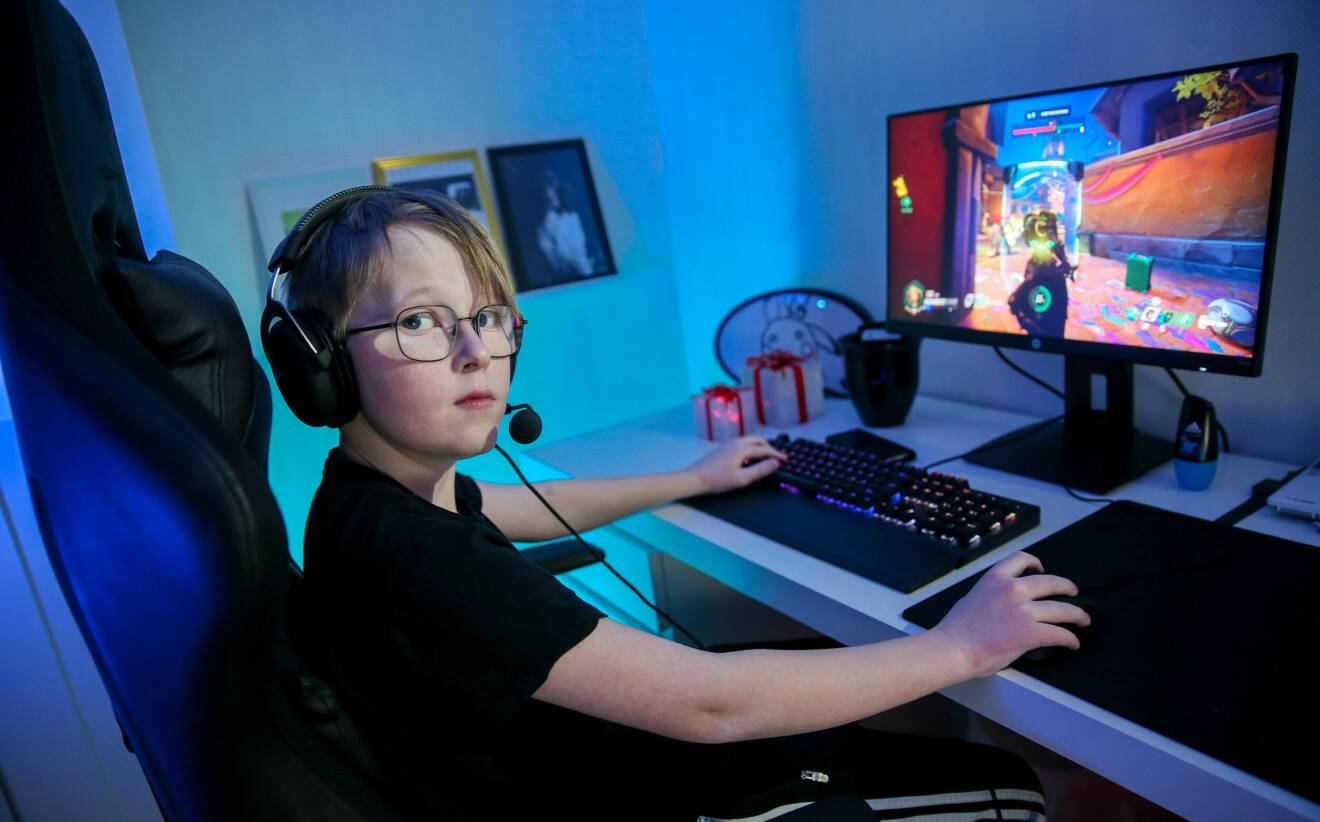 Bild på Oskar som sitter framför sin dator och spelar dataspel. Han har på sig hörlurar och tittar in i kameran.