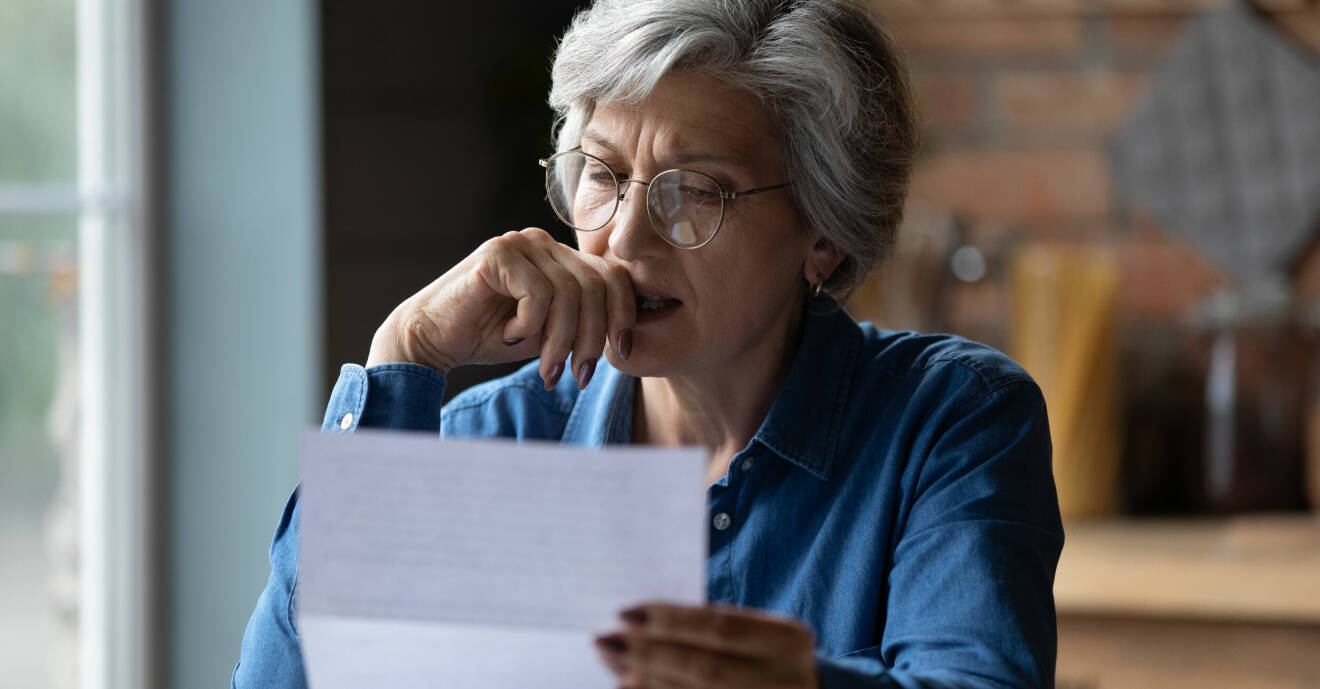 En kvinna med grått hår och glasögon läser ett brev.