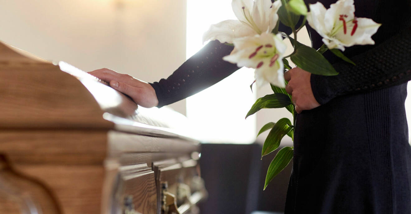 En kvinna står vid en kista med liljor i handen på en begravning.