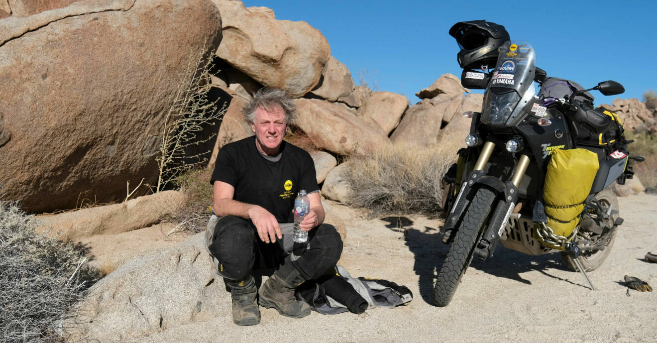 Nick Sanders sitter på en sten bredvid sin svarta motorcykel, i öknen i Mexiko.