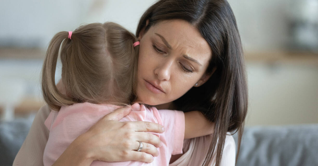 En bekymrad kvinna håller om ett litet barn i rosa tröja.