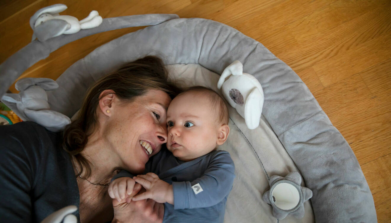 Lena Gavelin ligger på golvet och håller sin lilla son i händerna. Hon ler stort.