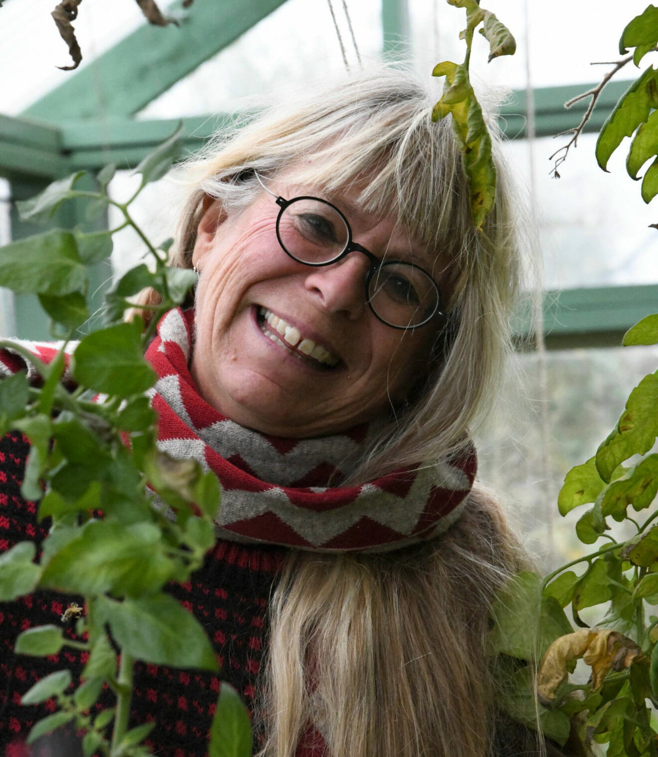 Eva står i ett växthus bland gröna blad. Hon har på sig mörka runda glasögon.