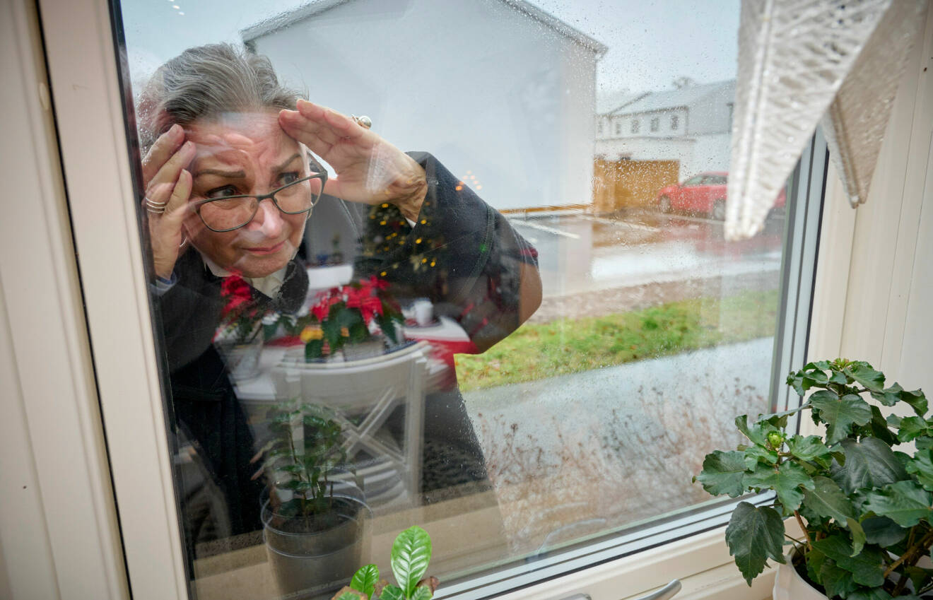 En kvinna tittar in genom ett fönster och ser orolig ut.