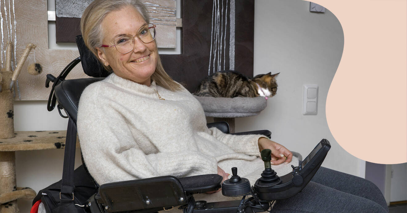 Anna Starck sitter i rullstol, hon har på sig en ljus stickad tröja och glasögon. Hennes katt sitter bakom henne.