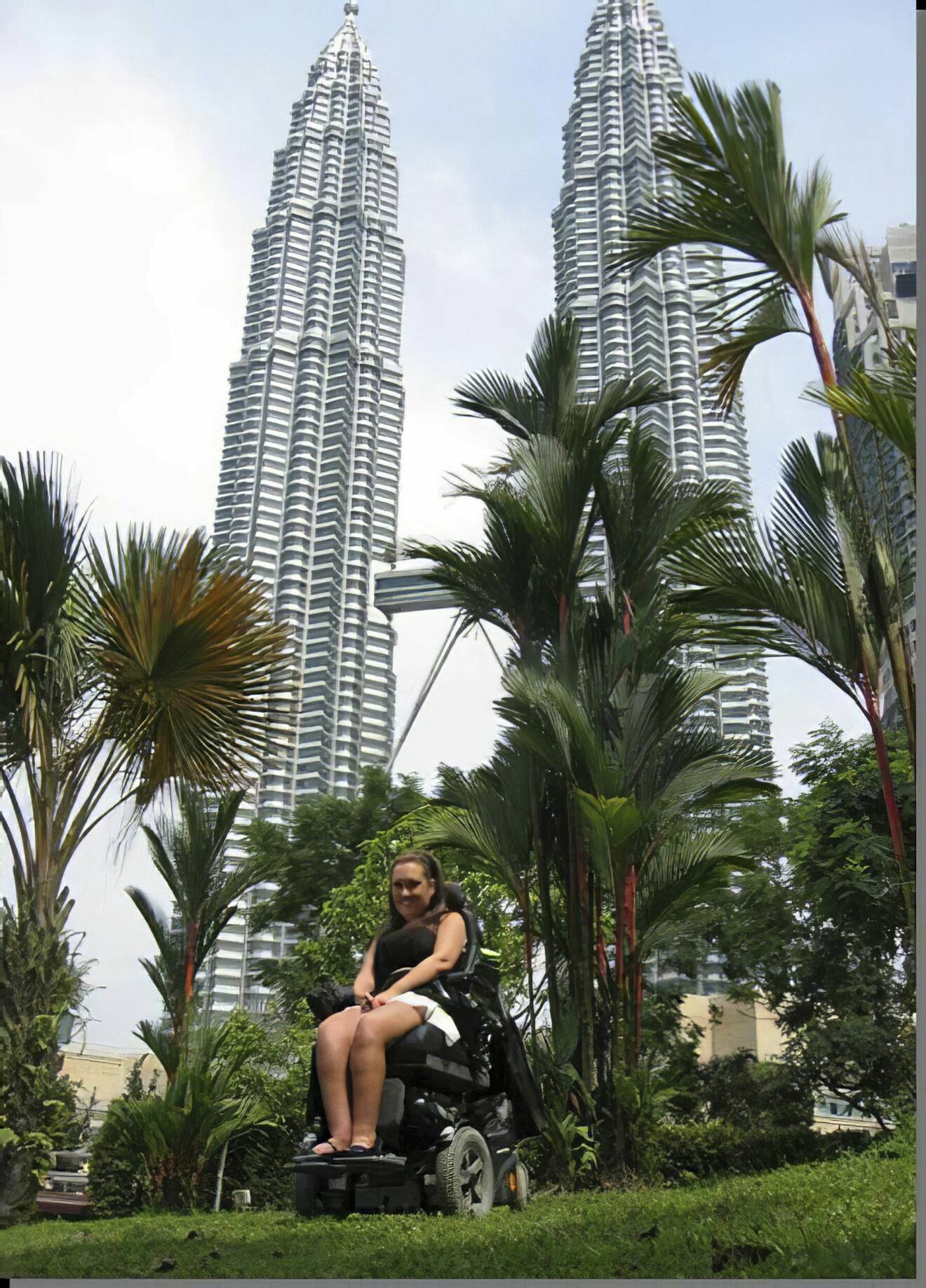Anna sitter i sin framför permobil Petronas Twin Towers i Kuala Lumpur.