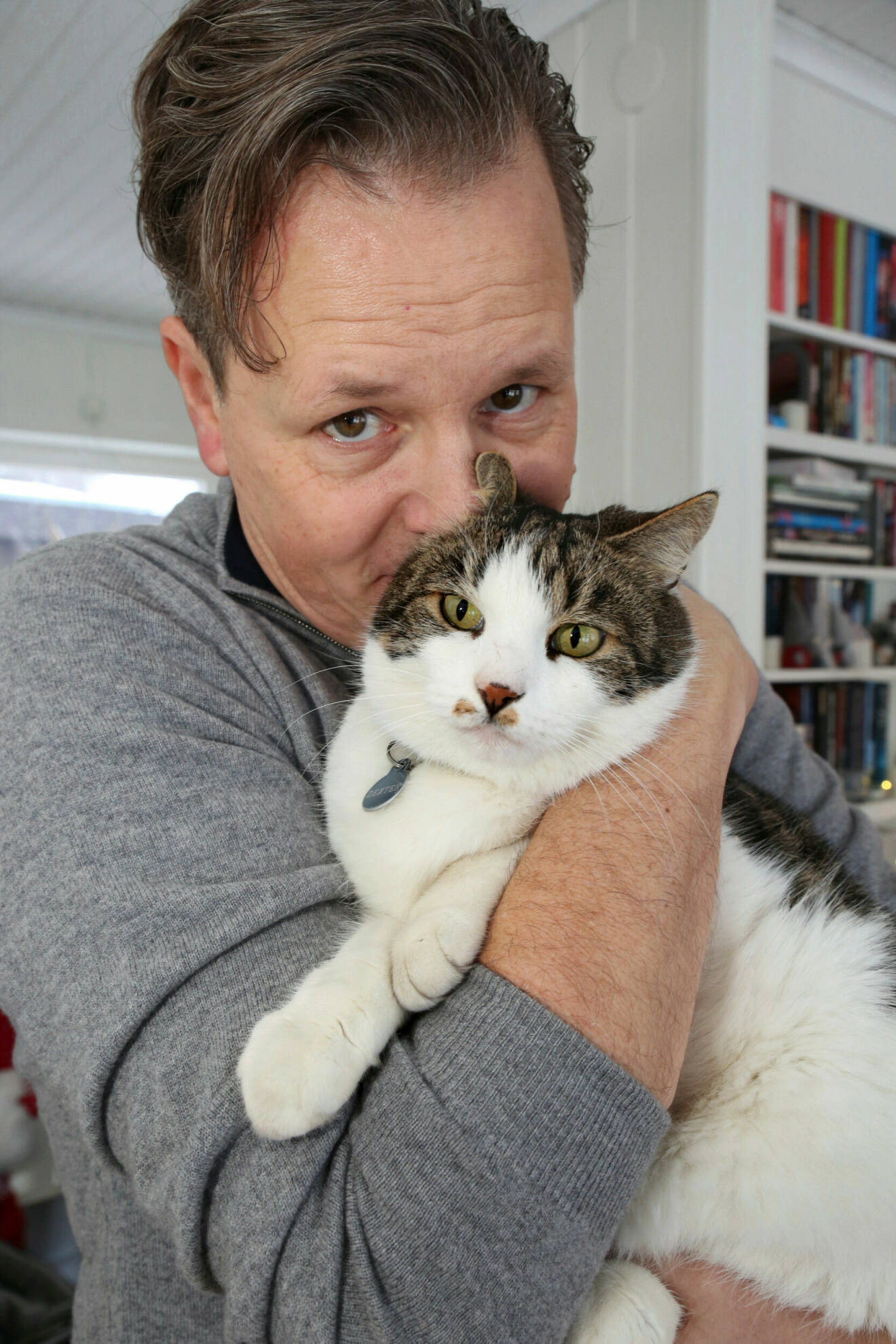 Husse Fredrik gosar med sin katt Dexter. Fredrik har på sig en grå tröja. Dexter är vit och brunspräcklig.