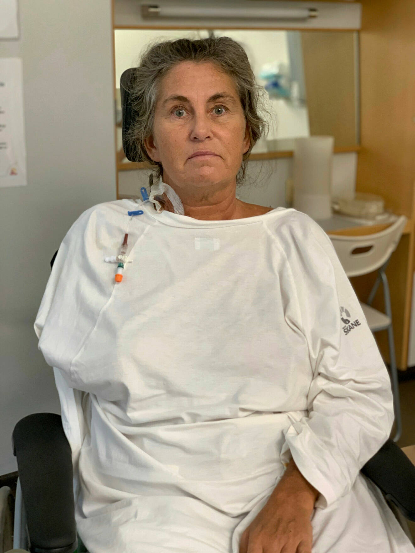 Gittel har grått uppsatt hår och har på sig i sjukhuskläder.