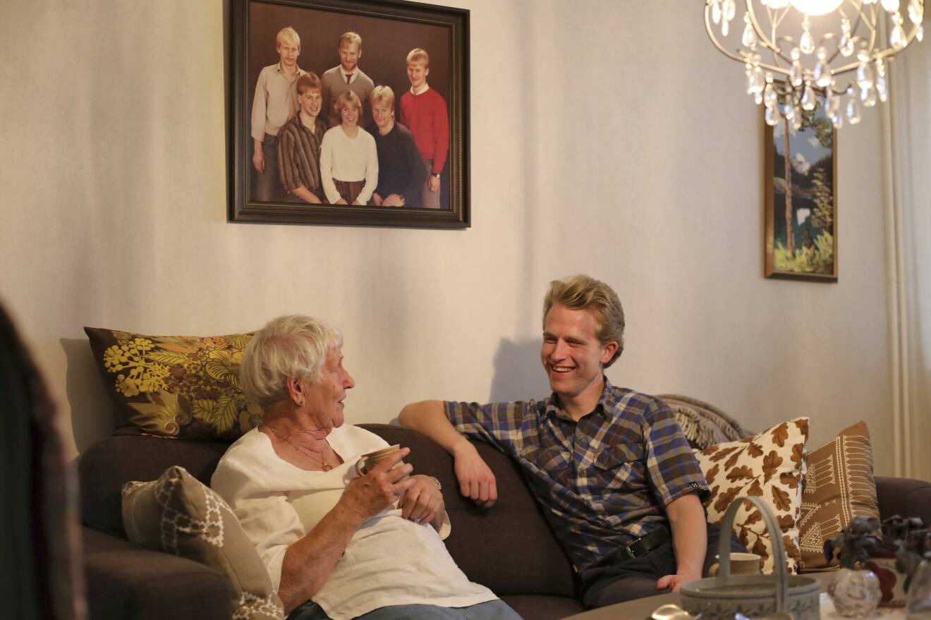 90-åriga Carin och 23-årige Emil sitter i soffan i Carins vardagsrum.