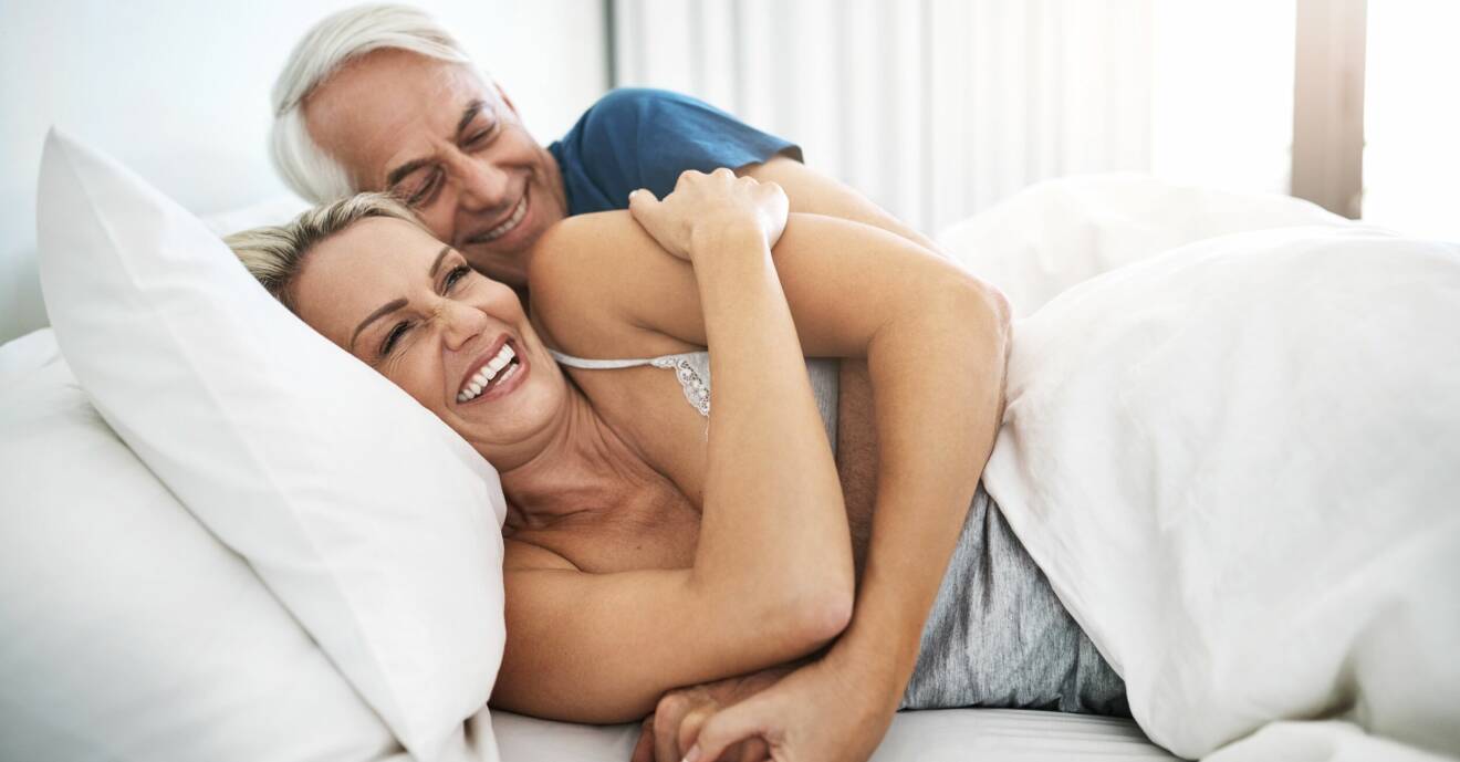 Ett par ligger i sängen och ler och håller om varandra.