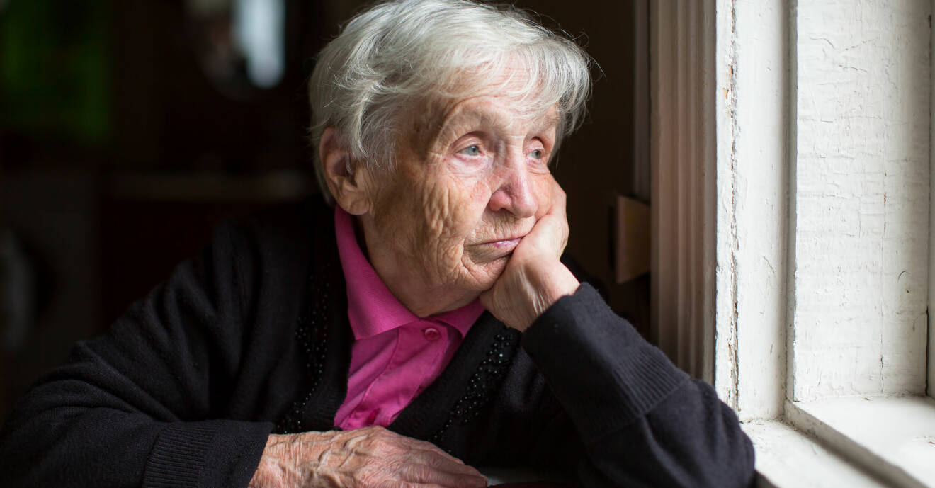 En gammal kvinna som tittar ut genom ett fönster