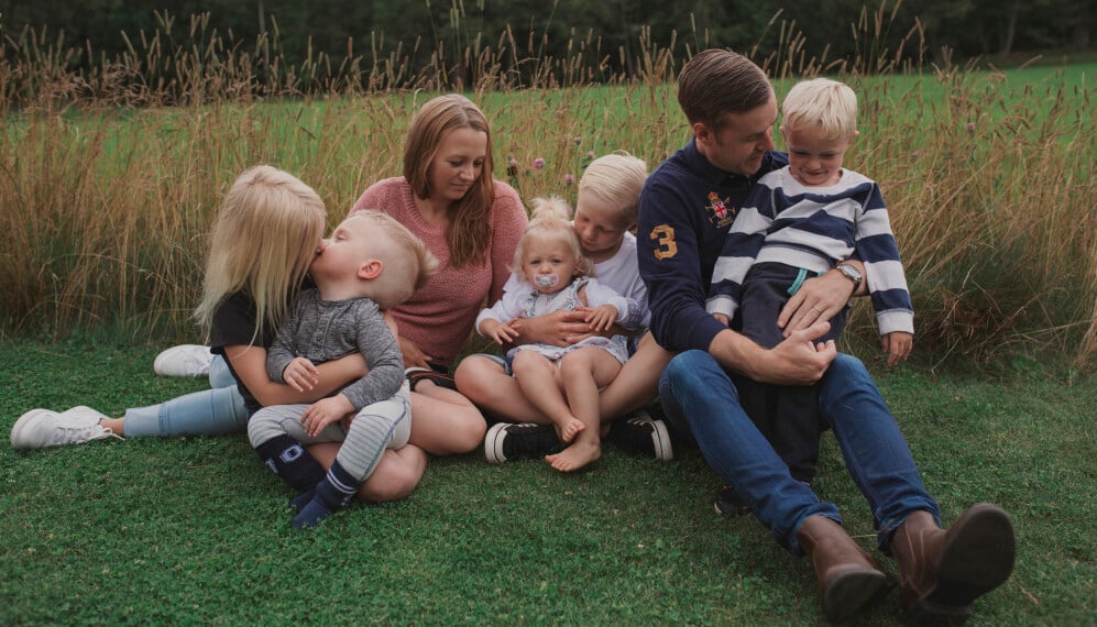 Familjen Bromander Sandén. Malin och hennes make Calle sitter vid en äng med fem barn.