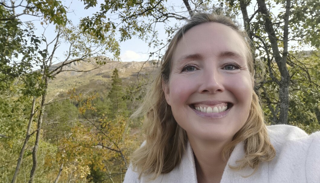 Porträttbild på Camilla som ler, hon står utomhus med grönt landskap bakom sig.