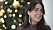 Porträttbild på Sofia. Hon har stora silvriga örhängen på sig och tittar ut ur bilden och ler. I bakgrunden syns en julgran.