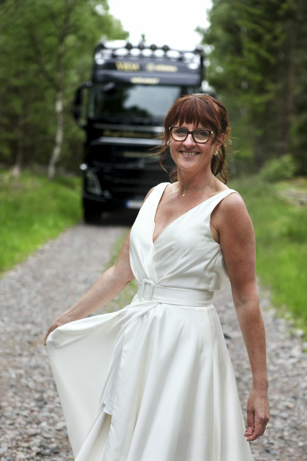 Inge Heimensen står i brusklänning på en grusväg med lastbilen i bakgrunden.